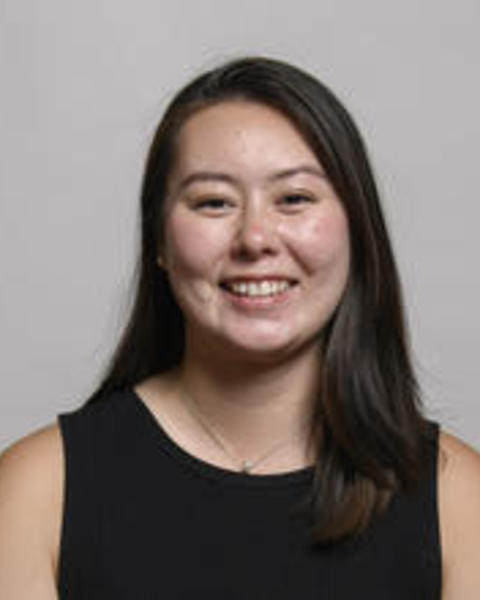 Tiara Borneman - smiling with long dark hair, black sleeveless shirt, grey background