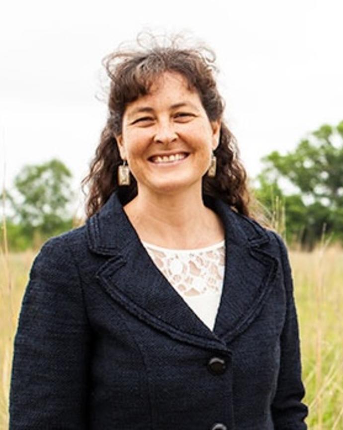Jeannine Cavender-Bares smiling, with long dark hair, standing in a field