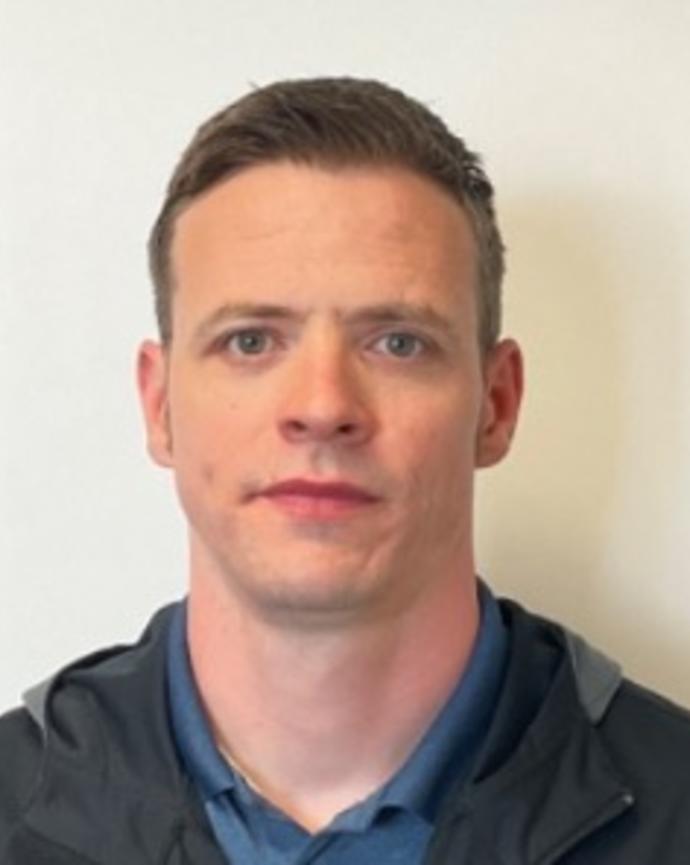 Portrait of James McKenna. Person with short dark hair wearing a black jacket and blue shirt