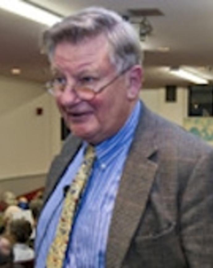 Peter Ashton wearing blue shirt, yellow tie, and a blazer, in classroom