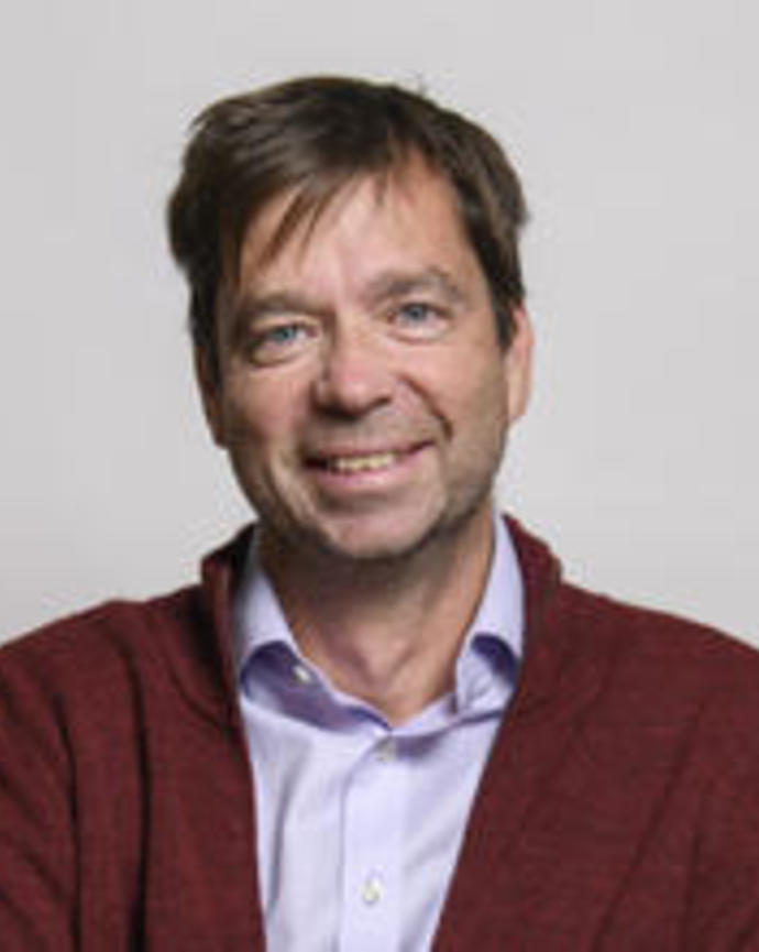 Bence Olveczky smiling, with short brown hair, a light purple shirt, and dark red sweater