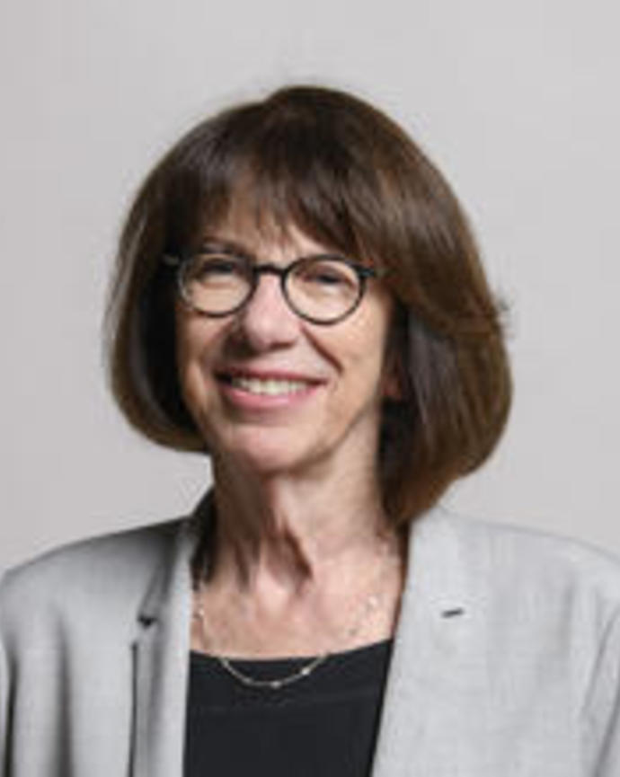 Colleen Cavanauth with medium dark hair wearing glasses, a black top and grey jacket in front of grey background