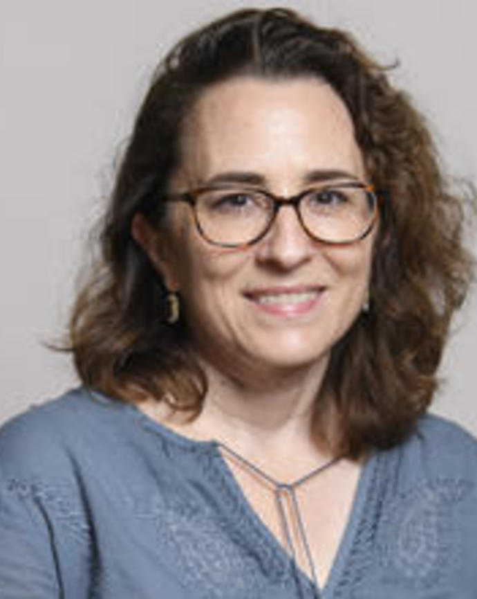 Elena Kramer smiling, with long dark hair, glasses, and wearing a blue shirt, in front of grey background