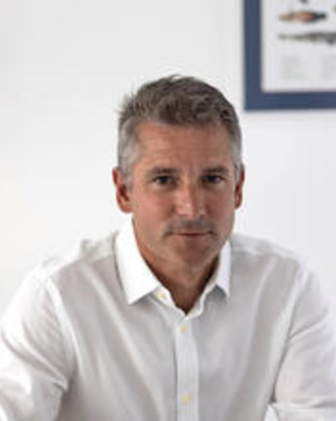 Gonzalo Giribet sitting, with short hair, wearing white button down, in front of white wall with framed picture