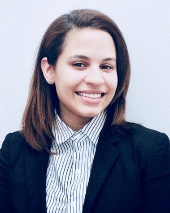 Janelle Batista, smiling, with long dark hair, striped button down, dark blazer, and light grey background