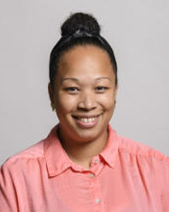 Liliana Teixeira-Davis with dark hair in high bun, peach shirt, grey background