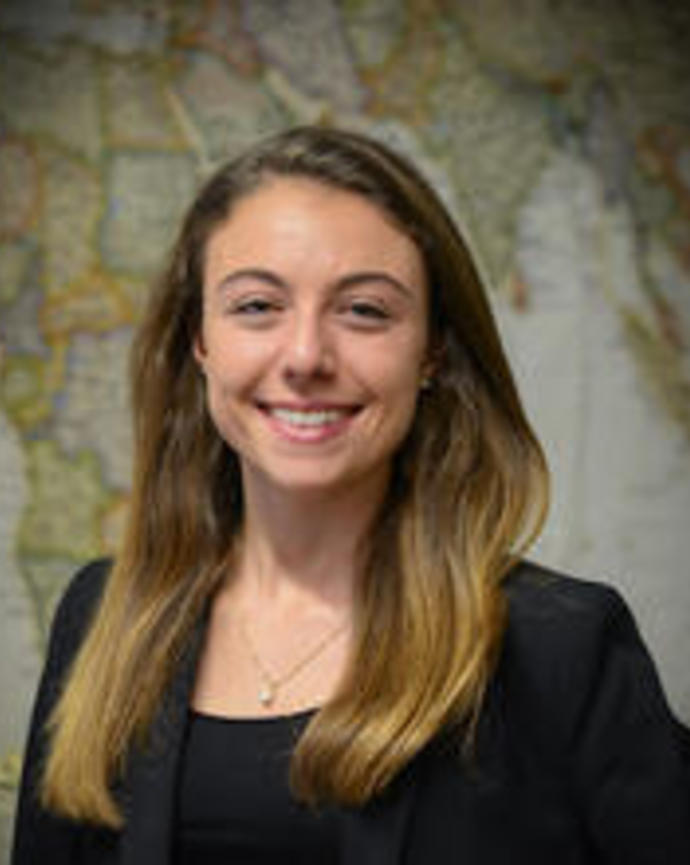 Lucrecia Aguilar with long light brown hair, wearing dark top and blazer, in front of world map
