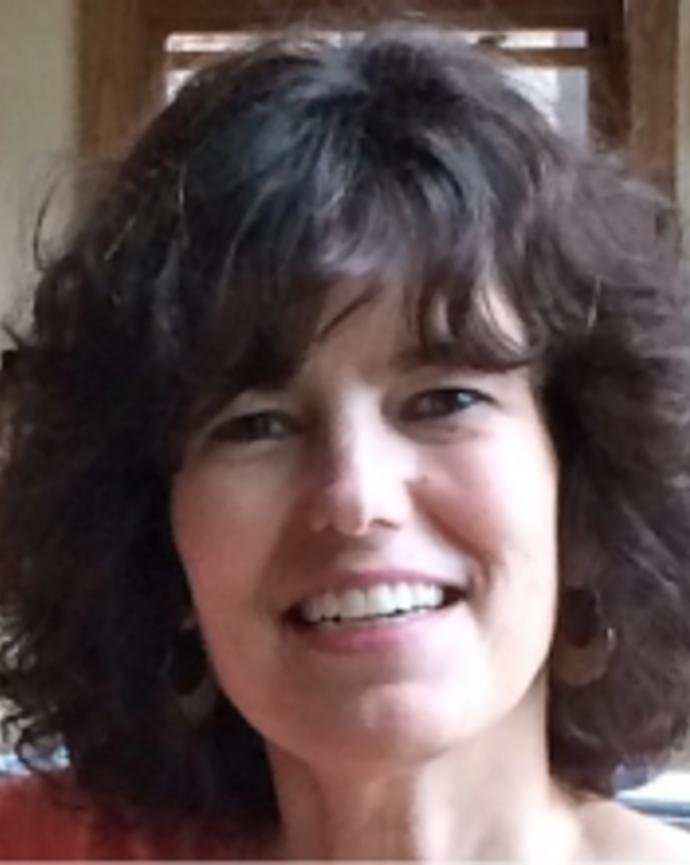 Lydia Carmosino with mediuem dark wavy hair and bangs, framed wall behind her