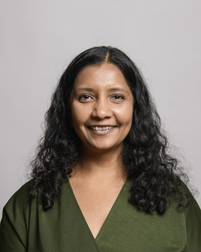 Mansi Srivistava with long, brown hair wearing a green blouse, in front of grey background
