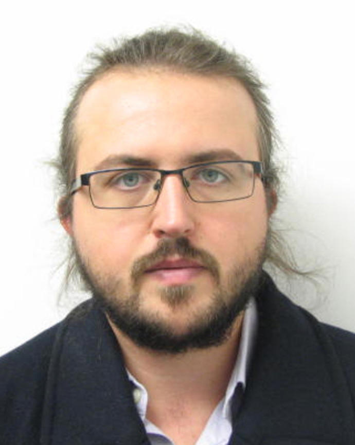 Pawel Zmarz with light brown hair and beard, glasses, and dark coat, in front of white background