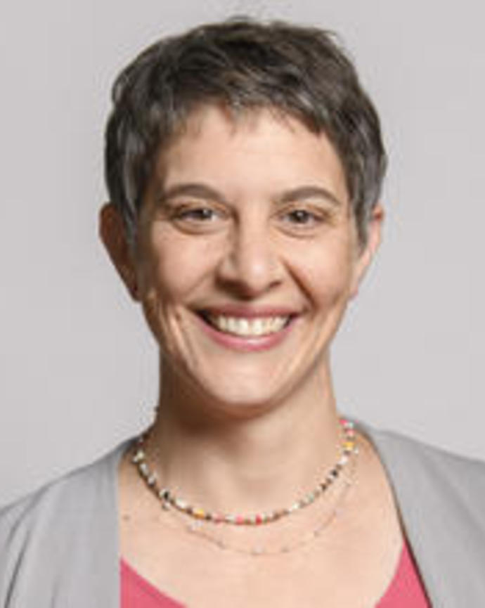 Robin Hopkins smiling, with short hair, grey sweater and pink top, in front of light grey background