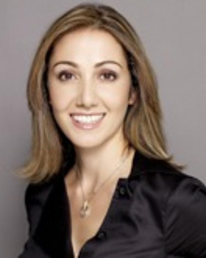 Pardis Sabeti smiling, with long light brown hair and black shirt, in front of grey background