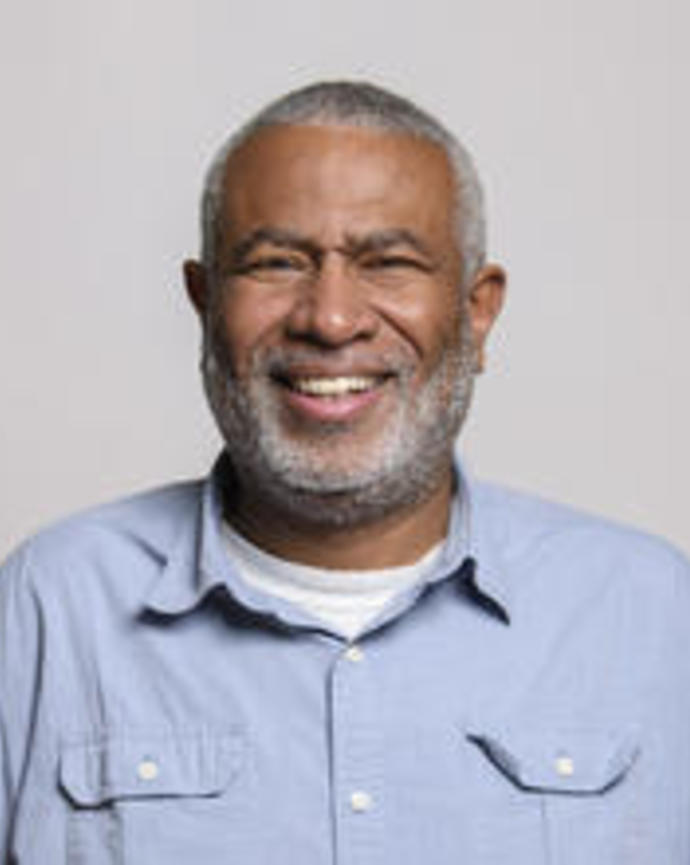 Scott Edwards smiling, with short grey hair and beard, wearing light blue button down, with light grey background