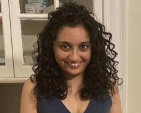 Shraddha Lall with long, curly dark hair, wearing blue sleevless top, in front of whitecabinet
