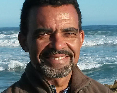 Man with beard wearing a jacket and standing in front of the ocean