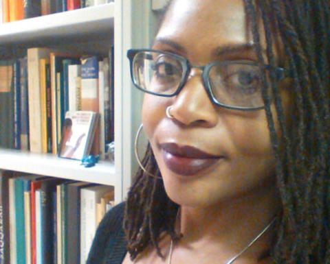 Woman with braids wearing glasses standing by a bookshelf