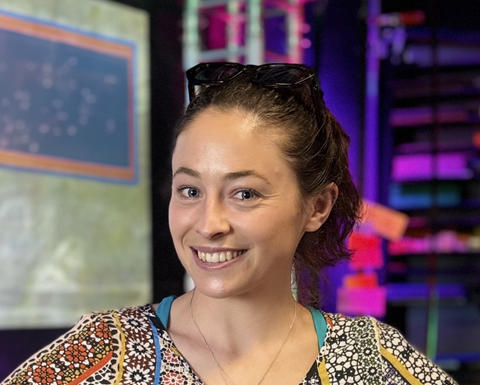 Graduate student Arianna Lord wearing sunglasses standing in front of a colorful background and smiling