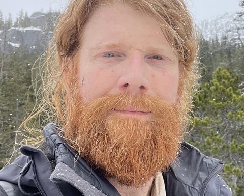 Man with beard wearing a black coat standing outside