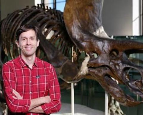 Man with crossed arms wearing a red checked shirt standing in front of a fossil